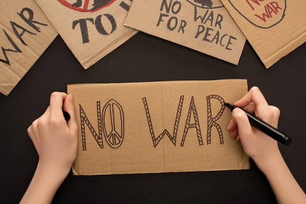 Cropped view of woman drawing placard with no war lettering on black background — Stock Photo