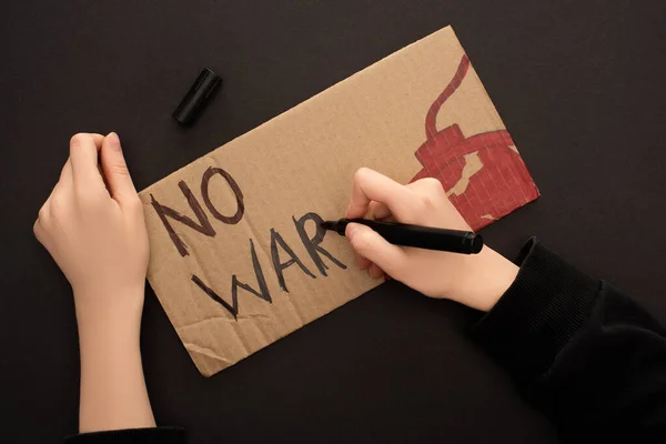 Cropped view of woman drawing placard with no war lettering and bomb on black background — Stock Photo