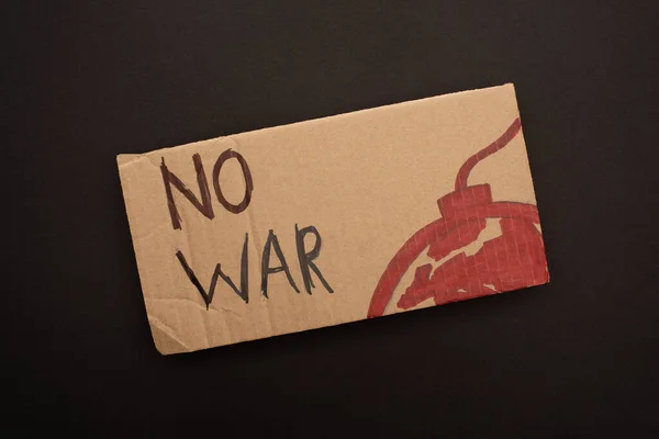 Top view of cardboard placard with no war lettering and bomb on black background — Stock Photo