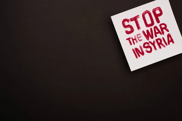 Top view of white placard with red stop war in Syria lettering on black background — Stock Photo