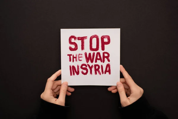 Vue recadrée d'une femme tenant une pancarte blanche avec inscription rouge stop war en Syrie sur fond noir — Photo de stock