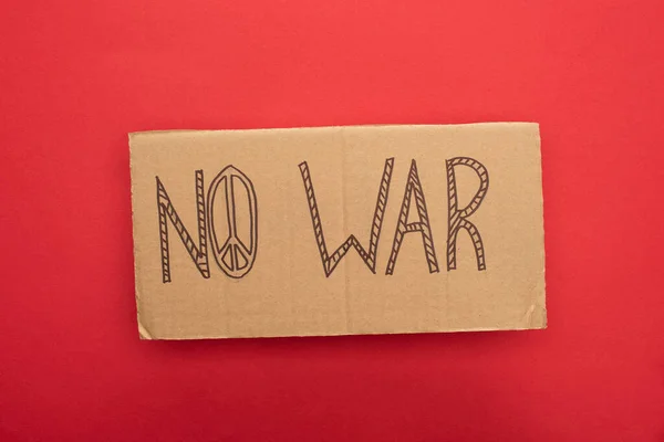 Top view of cardboard placard with no war lettering and peace sign on red background — Stock Photo