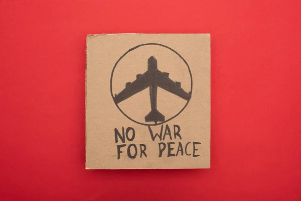Top view of cardboard placard with no war fro peace lettering and airplane on red background — Stock Photo