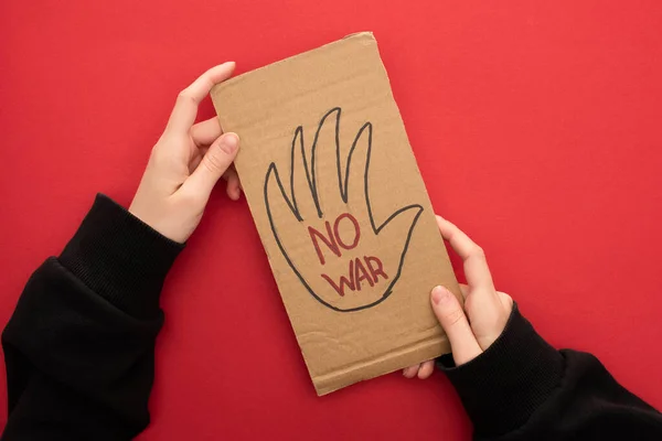 Top view of woman holding cardboard placard with no war lettering on red background — Stock Photo