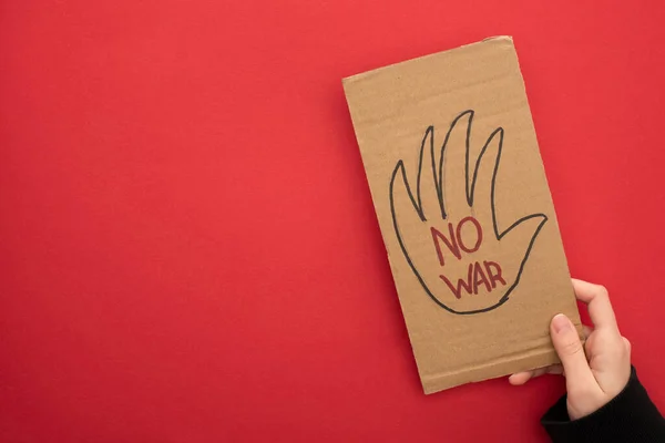 Top view of woman holding cardboard placard with no war lettering on red background — Stock Photo