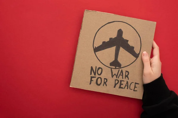 Обрізаний вид жінки, що тримає картонний плакат без війни для мирного написання та літака на червоному тлі — стокове фото