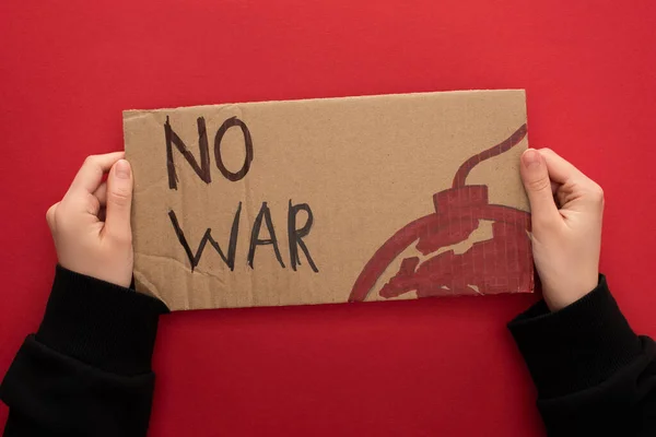 Vista cortada de mulher segurando cartaz de papelão sem letras de guerra e bomba no fundo vermelho — Fotografia de Stock