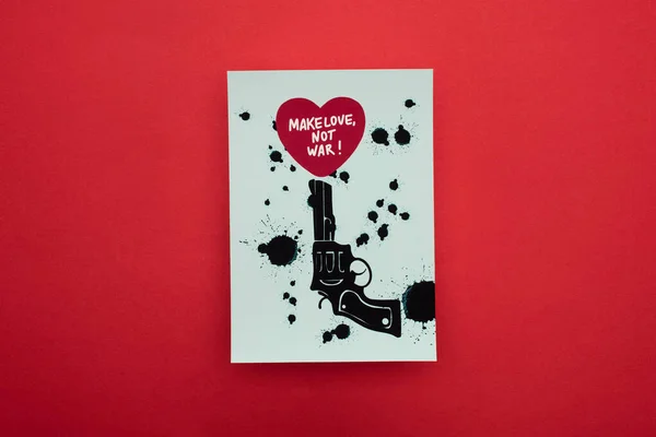 Visão superior do papel branco com revólver preto desenhado e coração com fazer amor não guerra lettering no fundo vermelho — Fotografia de Stock