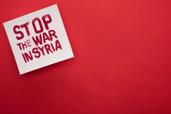 Vue du dessus de la plaque blanche avec inscription stop war in Syria sur fond rouge — Photo de stock