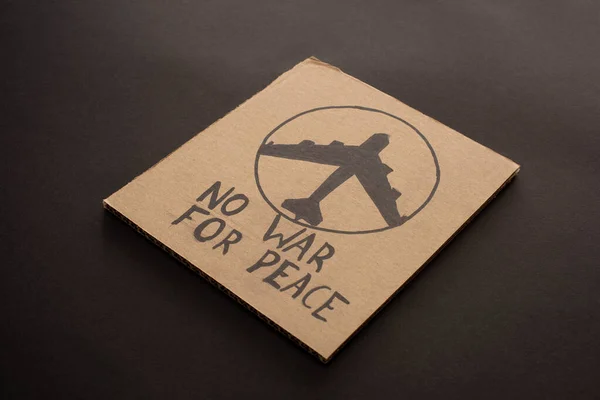 Cardboard placard with no war for peace lettering and airplane on black background — Stock Photo