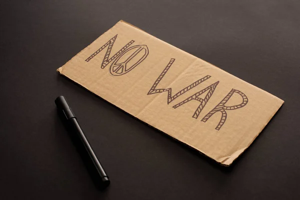 Cardboard placard with no war lettering and peace sign near marker on black background — Stock Photo