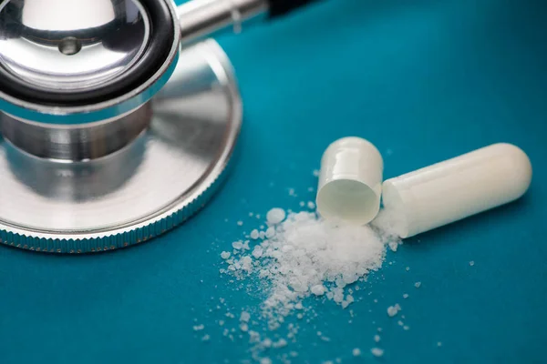 Close up view of probiotic capsule with white powder near stethoscope on blue background — Stock Photo