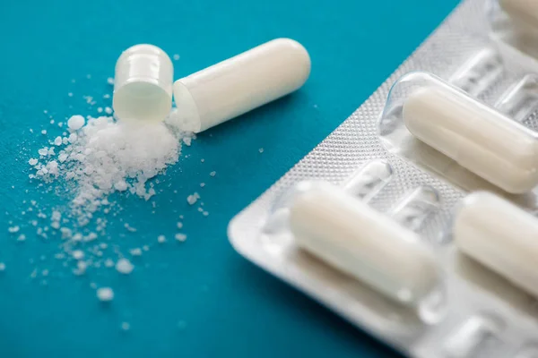 Close up view of probiotic capsules with white powder near blister pack on blue background — Stock Photo