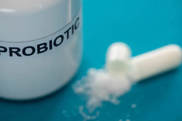 Selective focus of probiotic container near capsule with white powder on blue background — Stock Photo