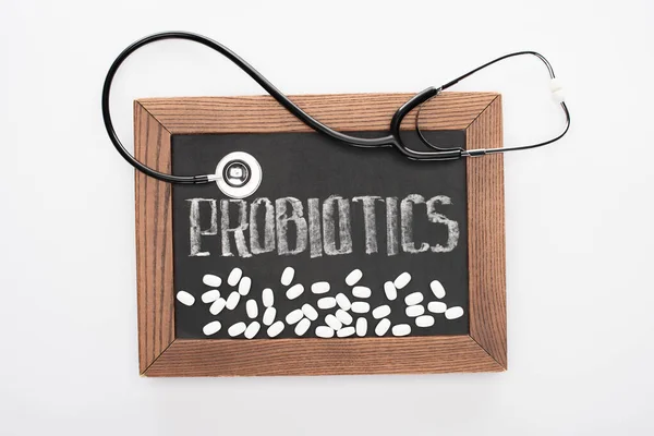 Vue du haut du tableau avec des probiotiques lettrage avec des pilules et stéthoscope sur fond blanc — Photo de stock