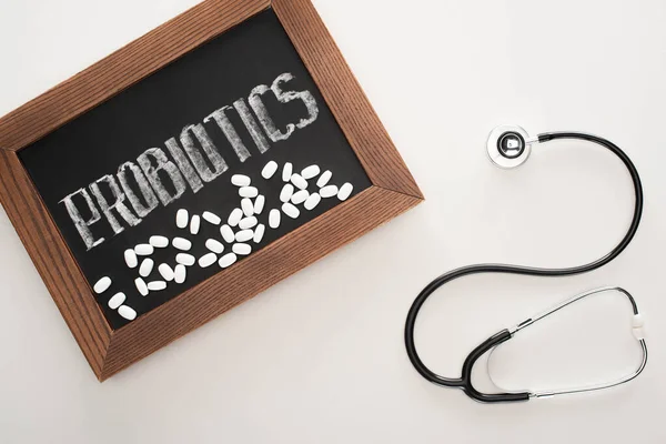 Top view of chalkboard with probiotics lettering with pills and stethoscope on white background — Stock Photo