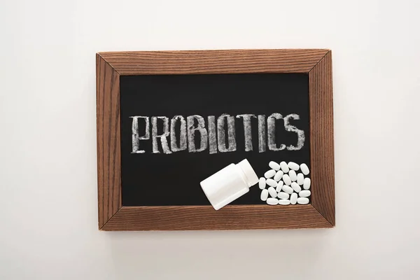 Top view of chalkboard with probiotics lettering with pills and container on white background — Stock Photo