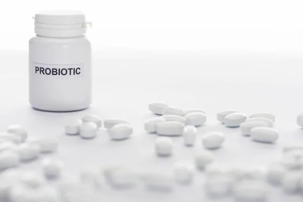 Foco seletivo de recipiente probiótico perto de pílulas em fundo branco — Fotografia de Stock
