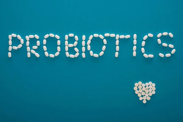 Vue du dessus des probiotiques lettrage et coeur fait de pilules sur fond bleu — Photo de stock