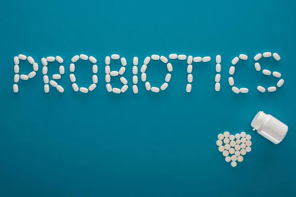 Top view of probiotics lettering and heart made of pills and container on blue background — Stock Photo