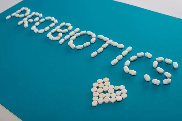 Probiotici lettering e cuore fatto di pillole su sfondo blu e bianco — Foto stock