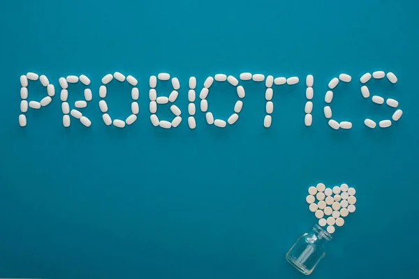 Top view of probiotics lettering and heart made of pills near glass jar on blue background — Stock Photo