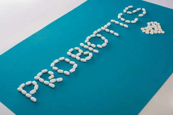 Probiotici lettering e cuore fatto di pillole su sfondo blu e bianco — Foto stock