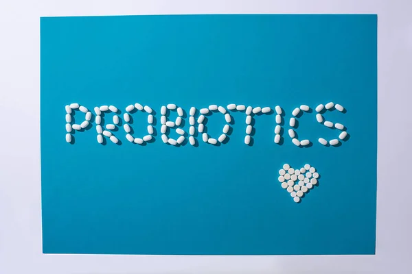 Top view of probiotics lettering and heart made of pills on blue and white background — Stock Photo