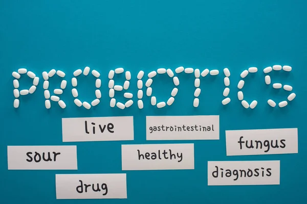 Top view of probiotics lettering made of pills near paper cards with words on blue background — Stock Photo