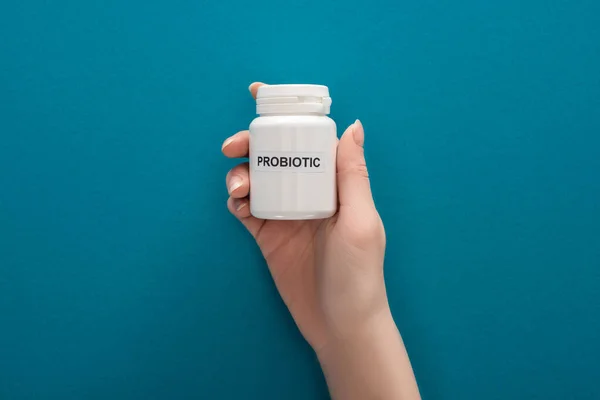 Cropped view of woman holding white probiotic container on blue background — Stock Photo