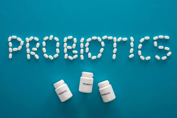 Vista superior de las letras de probióticos hechas de píldoras y recipientes sobre fondo azul - foto de stock