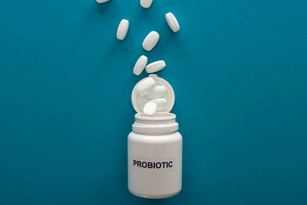 Vista superior del recipiente probiótico blanco con pastillas sobre fondo azul - foto de stock