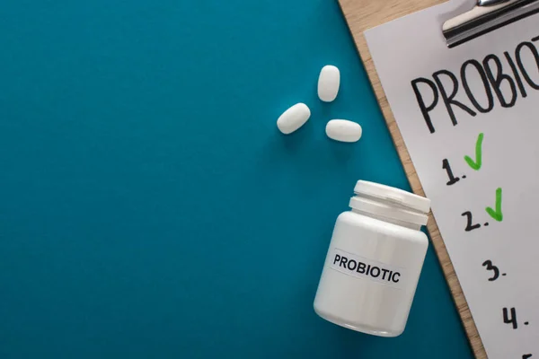 Top view of clipboard with probiotics empty list near container with pills on blue background — Stock Photo