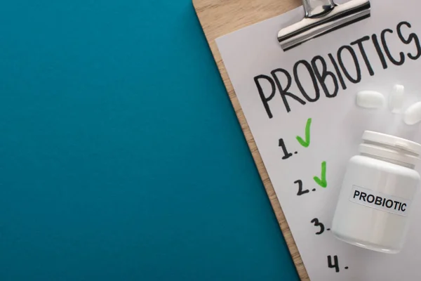 Top view of clipboard with probiotics empty list near container with pills on blue background — Stock Photo