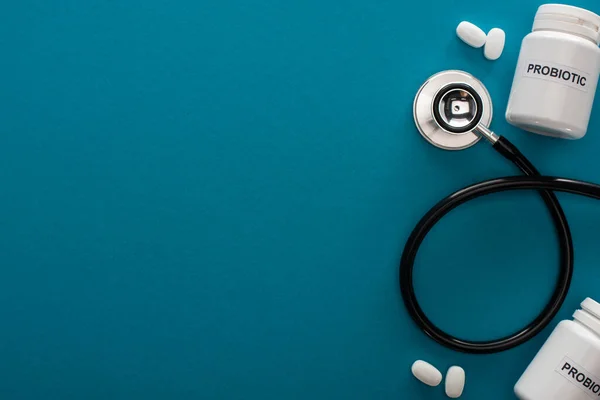 Top view of containers with probiotic lettering, pills and stethoscope on blue background — Stock Photo