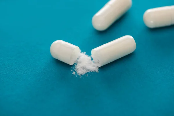 Close up view of probiotic capsules with white powder on blue background — Stock Photo