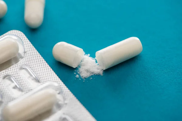 Close up view of probiotic capsules with white powder and blister pack on blue background — Stock Photo