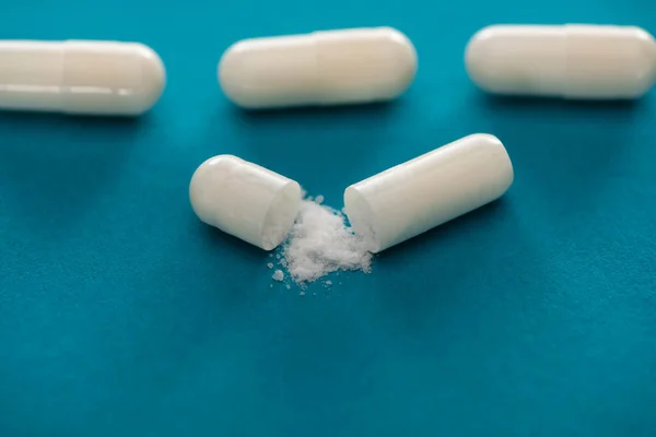 Close up view of probiotic capsules with white powder on blue background — Stock Photo