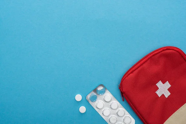 Top view of pills in blister pack and red first aid kit on blue background — Stock Photo