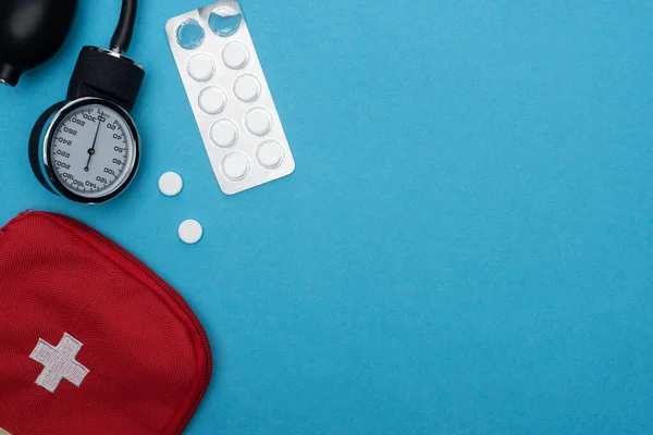 Top view of first aid kit, pills in blister pack and sphygmomanometer on blue background — Stock Photo