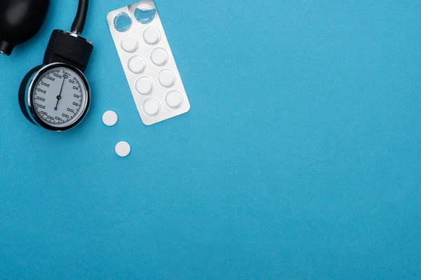 Вид таблеток в блистерной упаковке и сфигмоманометре на синем фоне — стоковое фото