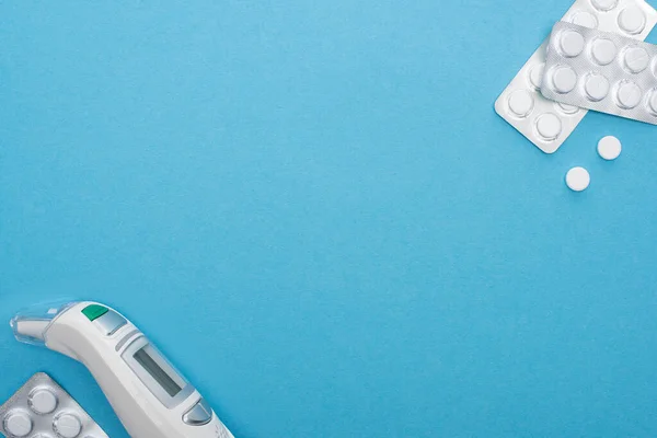 Top view of pills in blister packs and infrared thermometer on blue background — Stock Photo