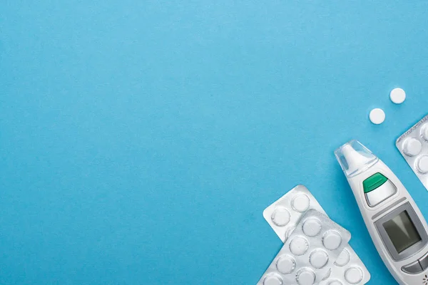 Top view of pills in blister packs and infrared thermometer on blue background — Stock Photo