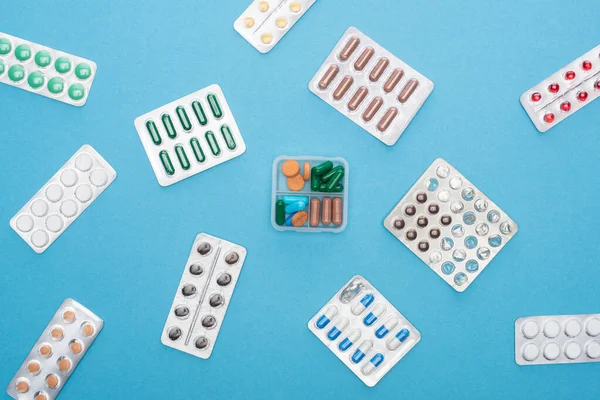 Top view of colorful pills in blister packs and plastic container on blue background — Stock Photo