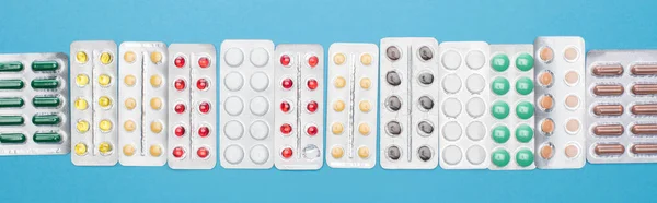 Vista superior de pílulas coloridas em embalagens blister em fundo azul, orientação panorâmica — Fotografia de Stock