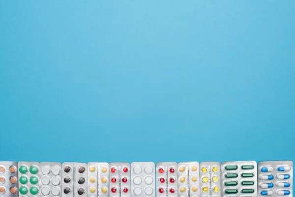 Top view of colorful pills in blister packs on blue background with copy space — Stock Photo