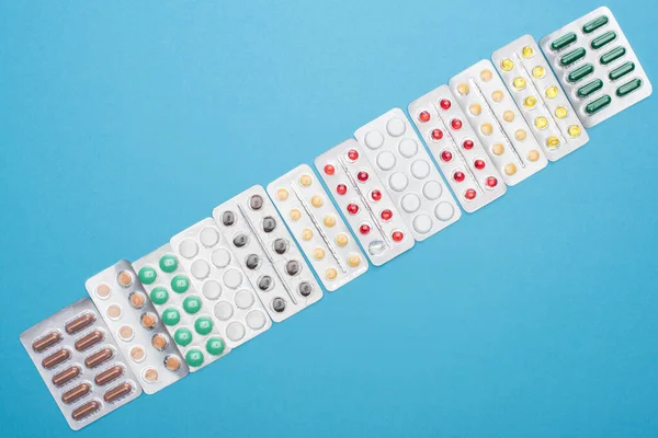 Vista dall'alto di pillole colorate in blister su sfondo blu — Foto stock