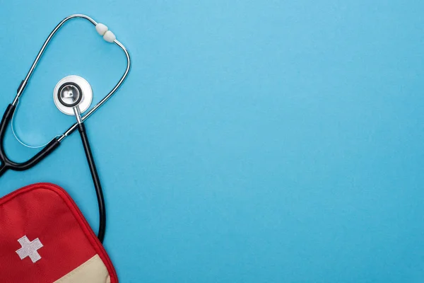 Vue du dessus de la trousse de premiers soins rouge et stéthoscope sur fond bleu — Photo de stock