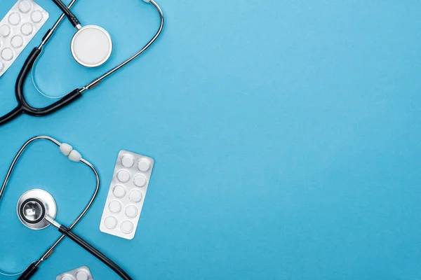 Top view of pills in blister packs and stethoscopes on blue background — Stock Photo