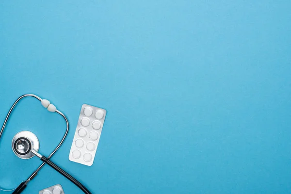 Top view of pills in blister packs and stethoscope on blue background — Stock Photo